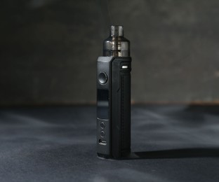Photo of One electronic smoking device on dark table against grey background, closeup