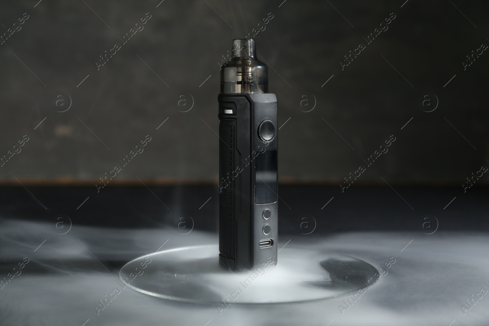 One electronic smoking device in smoke on dark table against grey background, closeup Photo of One electronic smoking device in smoke on dark table against grey background, closeup