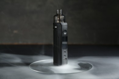 Photo of One electronic smoking device in smoke on dark table against grey background, closeup