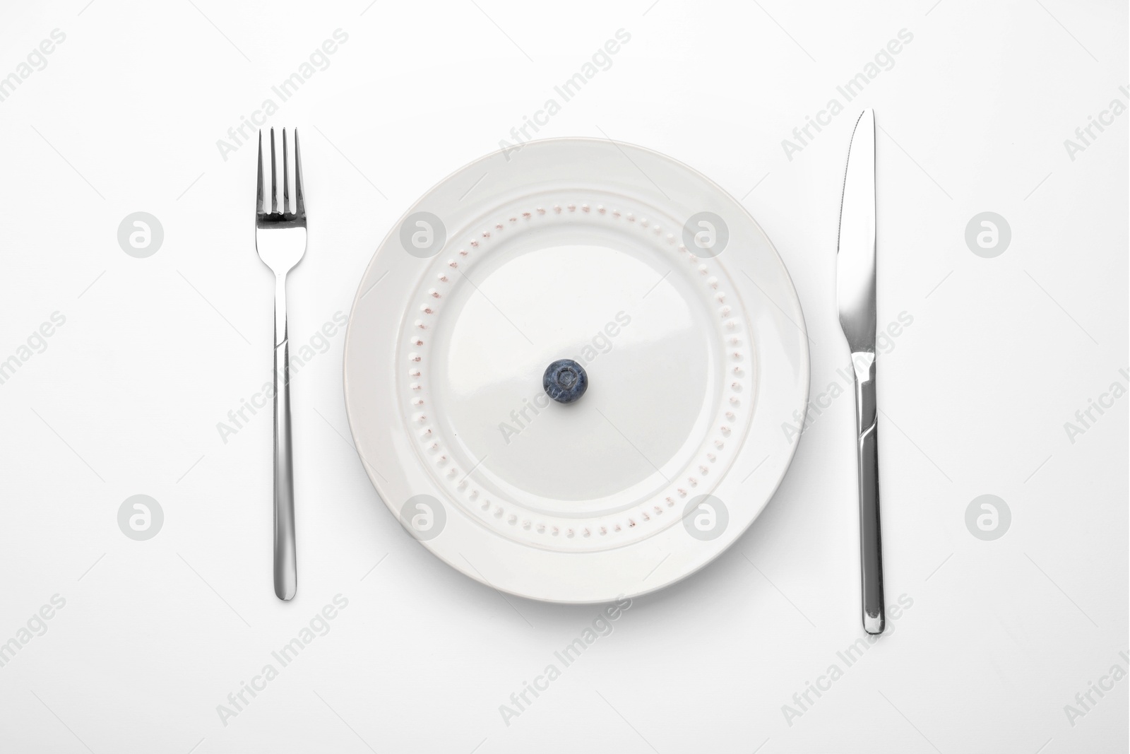 One blueberry on plate and cutlery on white table, flat lay Photo of One blueberry on plate and cutlery on white table, flat lay