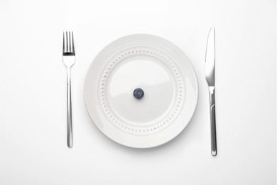 Photo of One blueberry on plate and cutlery on white table, flat lay