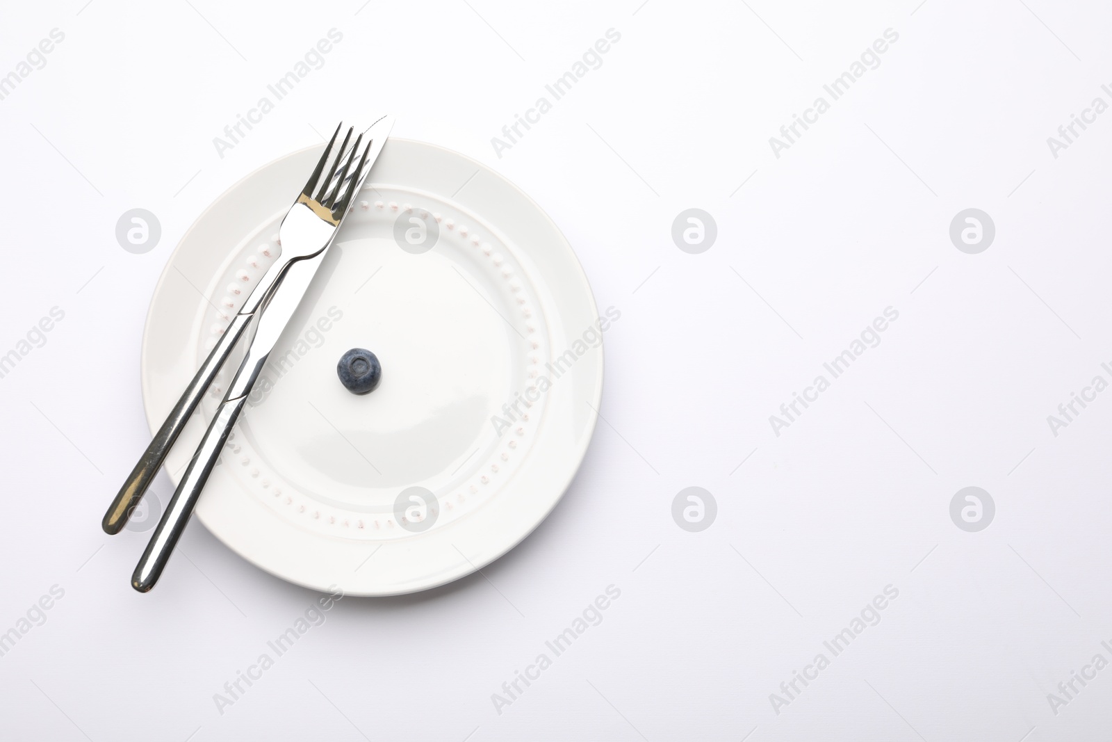One blueberry, cutlery and plate on white table, top view. Space for text Photo of One blueberry, cutlery and plate on white table, top view. Space for text