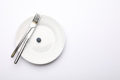 Photo of One blueberry, cutlery and plate on white table, top view. Space for text