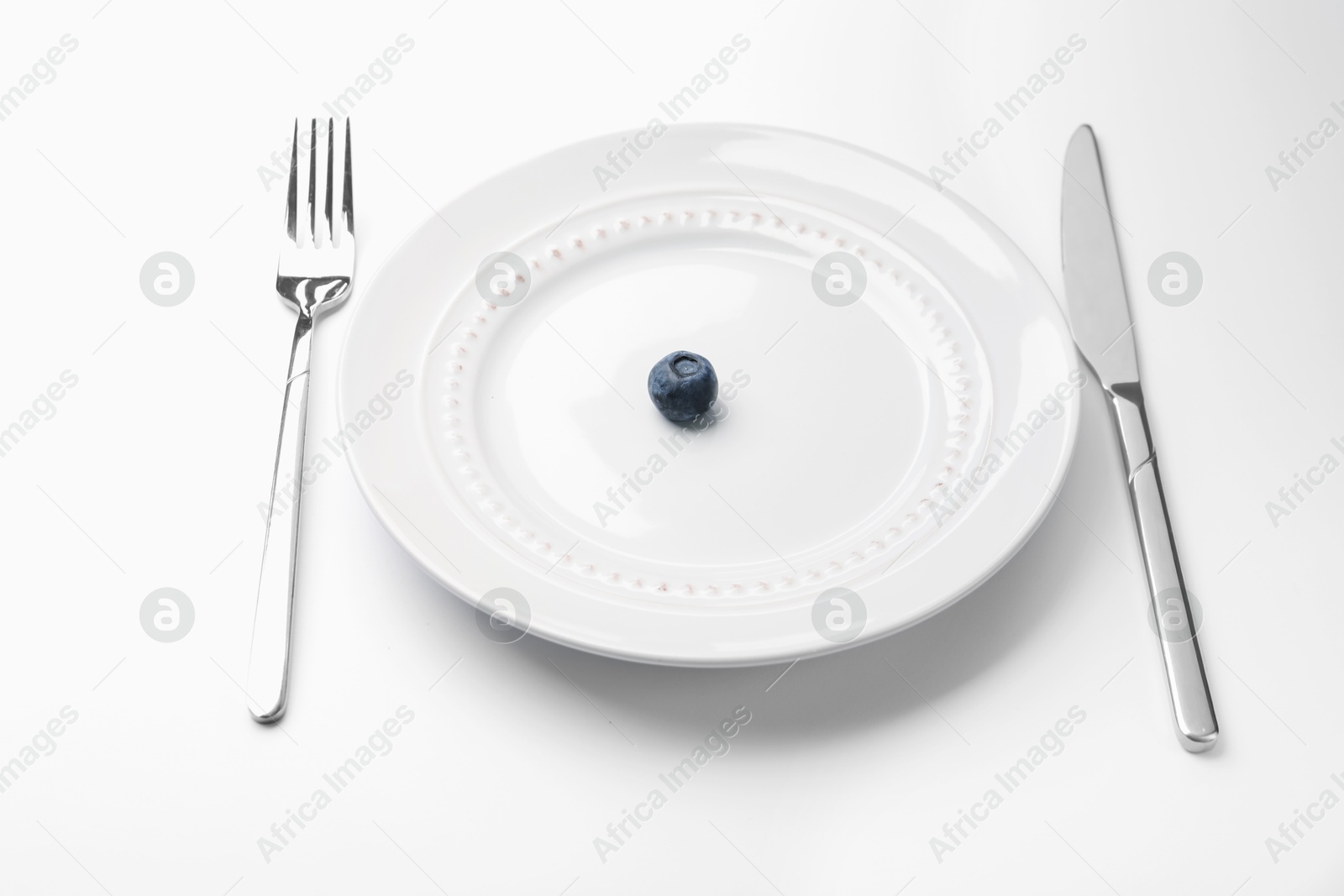 One blueberry on plate and cutlery on white table, closeup Photo of One blueberry on plate and cutlery on white table, closeup