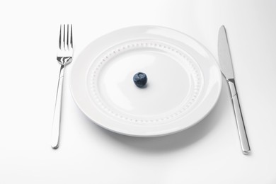 Photo of One blueberry on plate and cutlery on white table, closeup