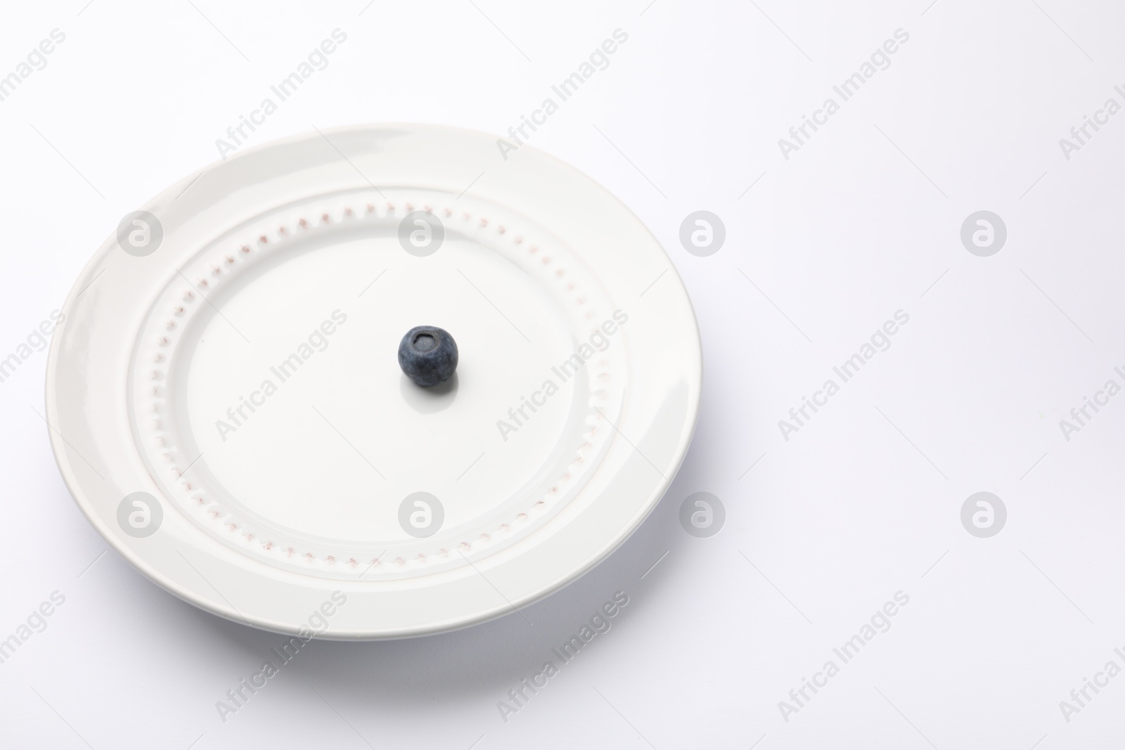 One blueberry and plate on white table, closeup. Space for text Photo of One blueberry and plate on white table, closeup. Space for text