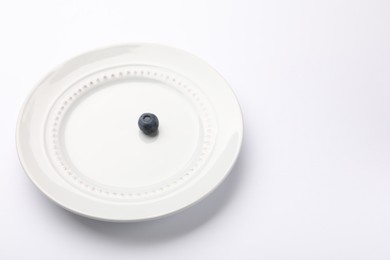Photo of One blueberry and plate on white table, closeup. Space for text