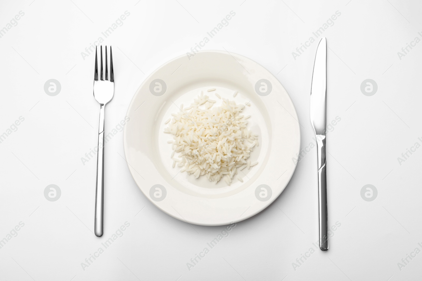Pile of rice, plate and cutlery on white table, flat lay Photo of Pile of rice, plate and cutlery on white table, flat lay