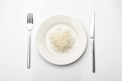 Photo of Pile of rice, plate and cutlery on white table, flat lay