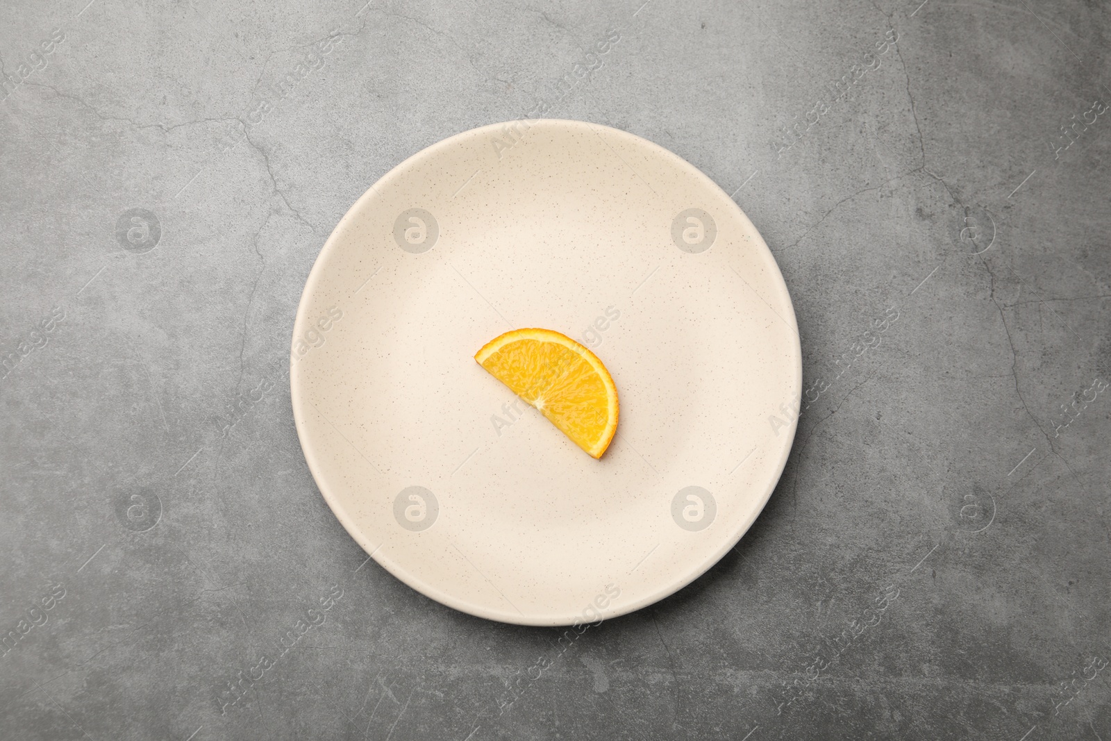 Slice of orange and plate on grey textured table, top view Photo of Slice of orange and plate on grey textured table, top view