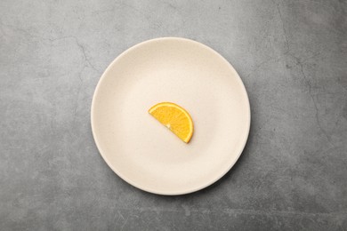 Photo of Slice of orange and plate on grey textured table, top view