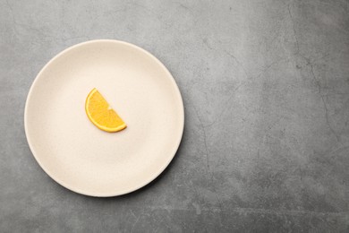 Photo of Slice of orange and plate on grey textured table, top view. Space for text