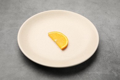 Photo of Slice of orange and plate on grey textured table, closeup