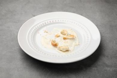 Photo of Dirty plate with crumbs and sauce on grey textured table, closeup