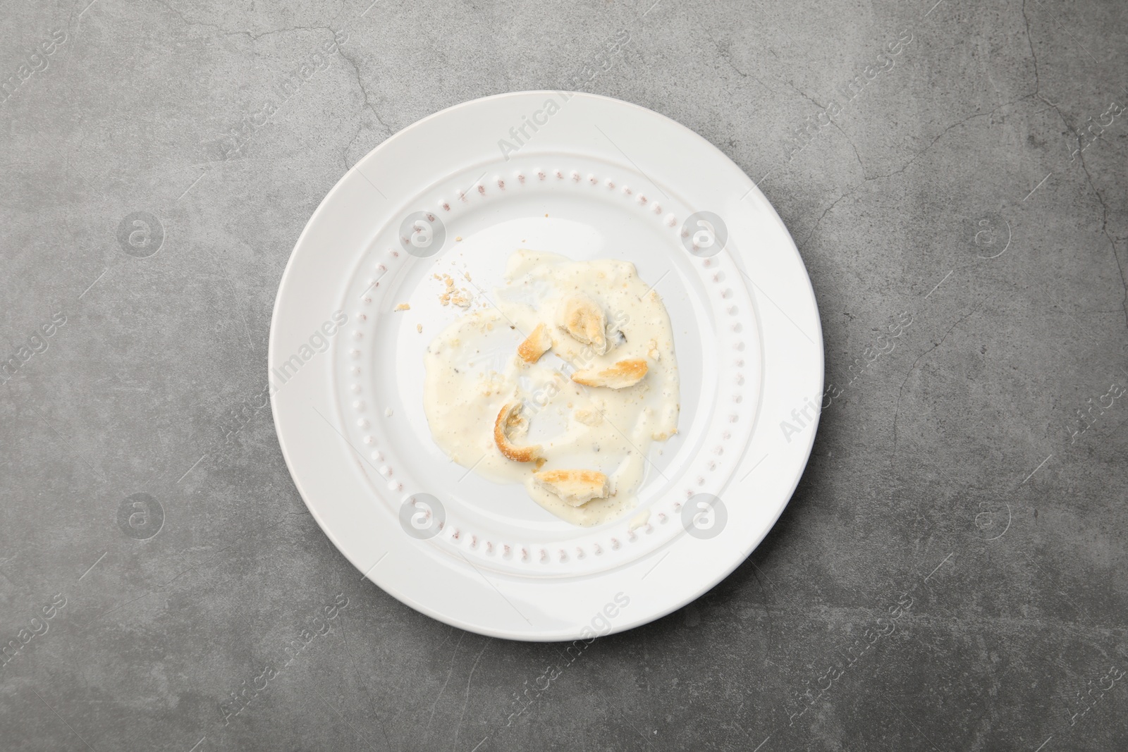 Dirty plate with crumbs and sauce on grey textured table, top view Photo of Dirty plate with crumbs and sauce on grey textured table, top view