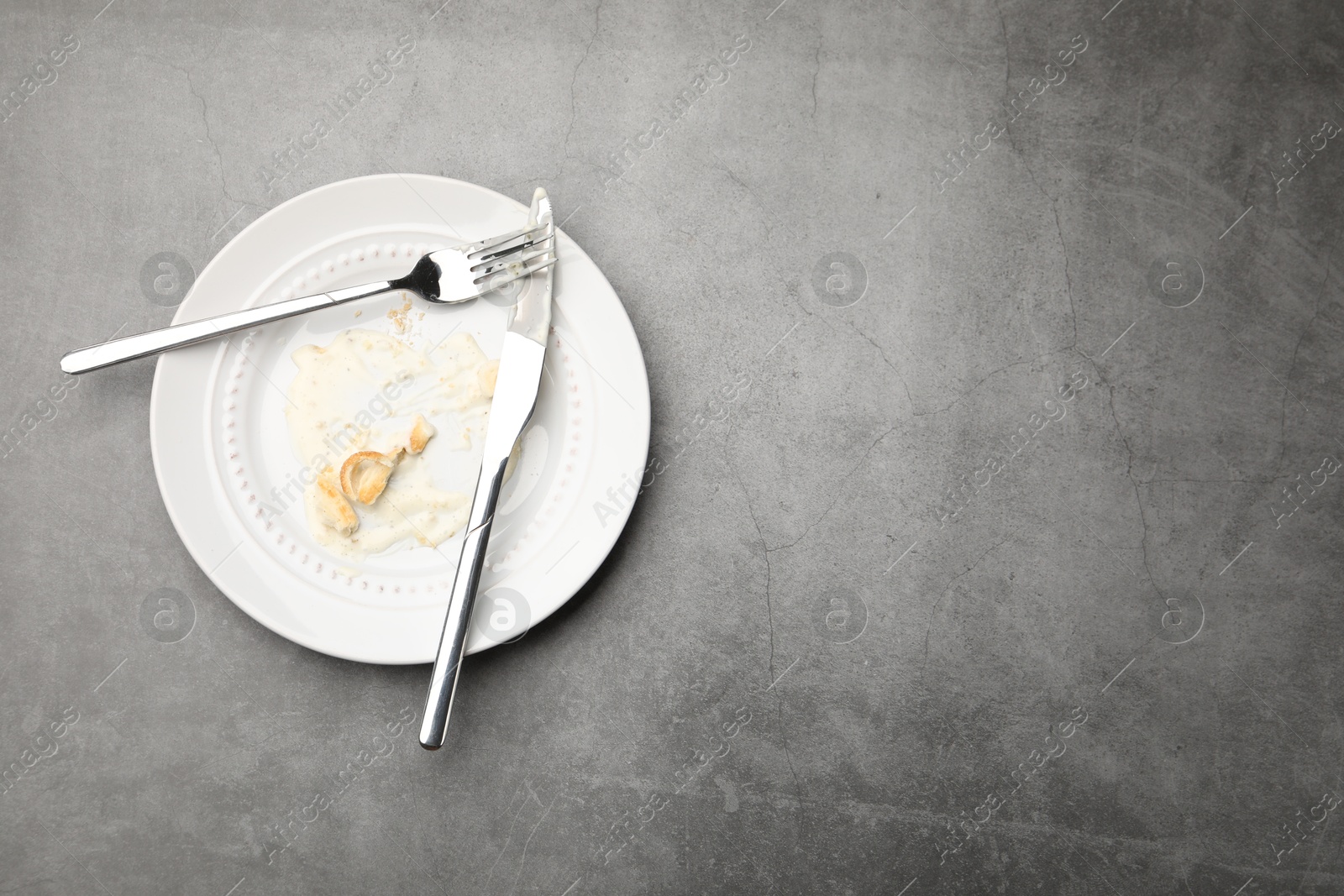 Dirty plate with crumbs, sauce and cutlery on grey textured table, top view. Space for text Photo of Dirty plate with crumbs, sauce and cutlery on grey textured table, top view. Space for text