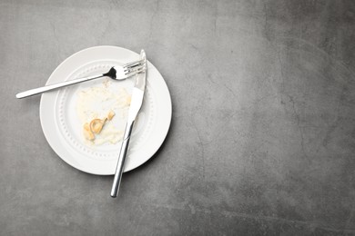 Photo of Dirty plate with crumbs, sauce and cutlery on grey textured table, top view. Space for text