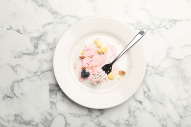 Photo of Dirty plate with crumbs, jam, blueberry and fork on white marble table, top view