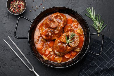 Photo of Tasty beef ossobuco with carrot and mushrooms served on dark textured table, flat lay