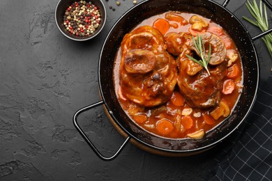 Photo of Tasty beef ossobuco with carrot and mushrooms on dark textured table, flat lay
