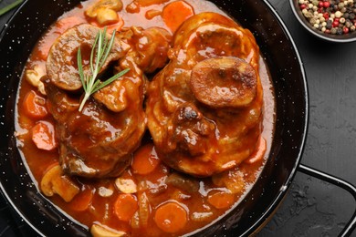 Photo of Tasty beef ossobuco with carrot and mushrooms on dark textured table, flat lay
