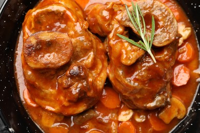 Photo of Tasty beef ossobuco with carrot, mushrooms and rosemary in frying pan, top view