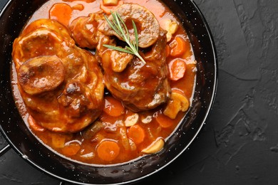 Photo of Tasty beef ossobuco with carrot, mushrooms and rosemary in frying pan on dark textured table, top view