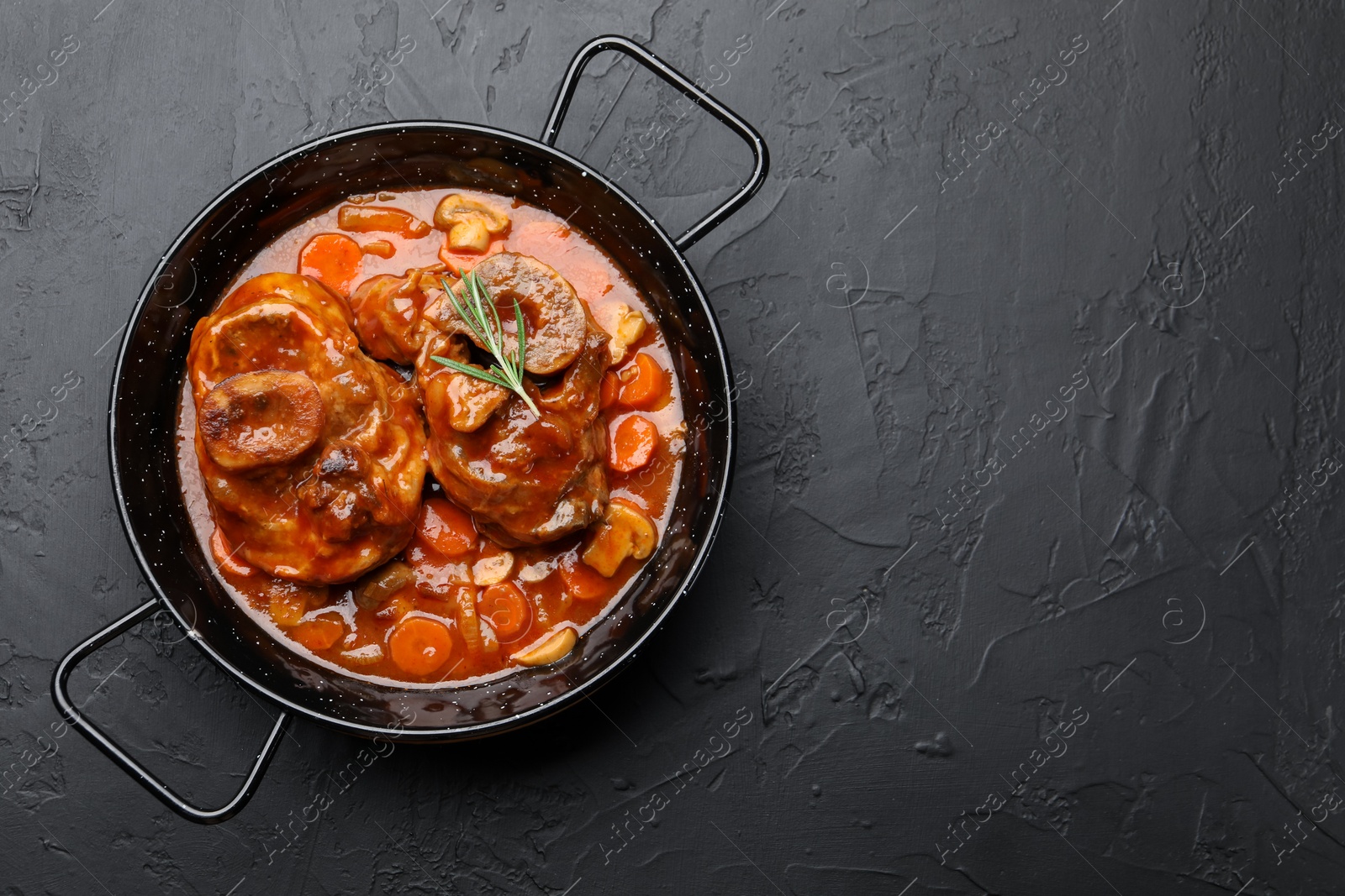Tasty beef ossobuco with carrot, mushrooms and rosemary in frying pan on dark textured table, top view. Space for text Photo of Tasty beef ossobuco with carrot, mushrooms and rosemary in frying pan on dark textured table, top view. Space for text