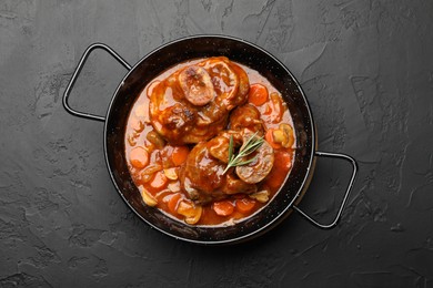 Photo of Tasty beef ossobuco with carrot, mushrooms and rosemary in frying pan on dark textured table, top view