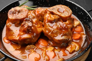Photo of Tasty beef ossobuco with carrot, mushrooms and rosemary in frying pan on table, closeup