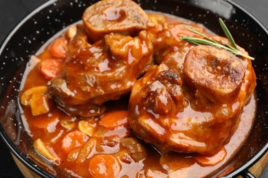 Photo of Tasty beef ossobuco with carrot, mushrooms and rosemary in frying pan on table, closeup