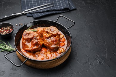 Photo of Tasty beef ossobuco with carrot, mushrooms and rosemary in frying pan on dark textured table, closeup