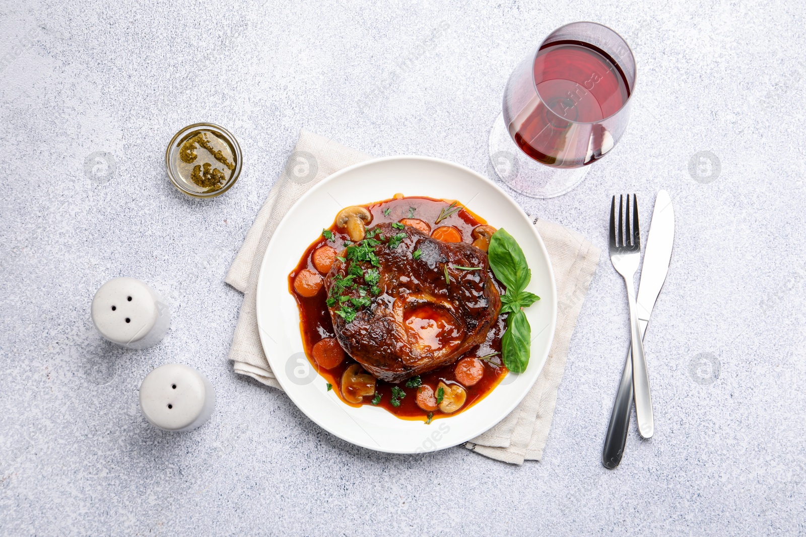Tasty beef ossobuco with carrot, mushrooms and herbs served on grey textured table, flat lay Photo of Tasty beef ossobuco with carrot, mushrooms and herbs served on grey textured table, flat lay