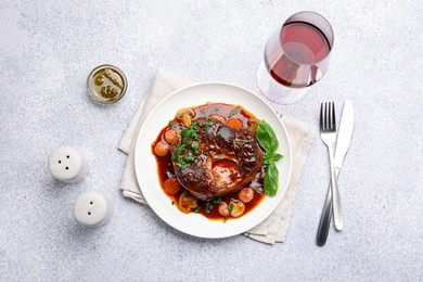 Photo of Tasty beef ossobuco with carrot, mushrooms and herbs served on grey textured table, flat lay