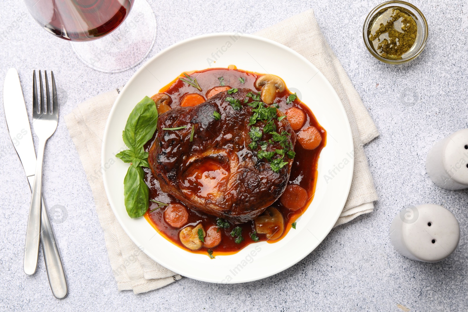 Tasty beef ossobuco with carrot, mushrooms and herbs served on grey textured table, flat lay Photo of Tasty beef ossobuco with carrot, mushrooms and herbs served on grey textured table, flat lay