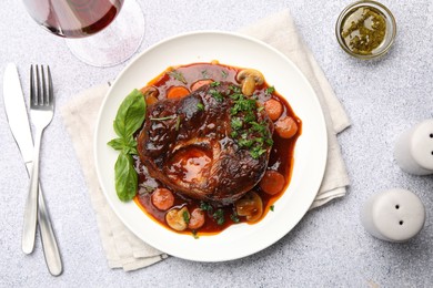 Photo of Tasty beef ossobuco with carrot, mushrooms and herbs served on grey textured table, flat lay