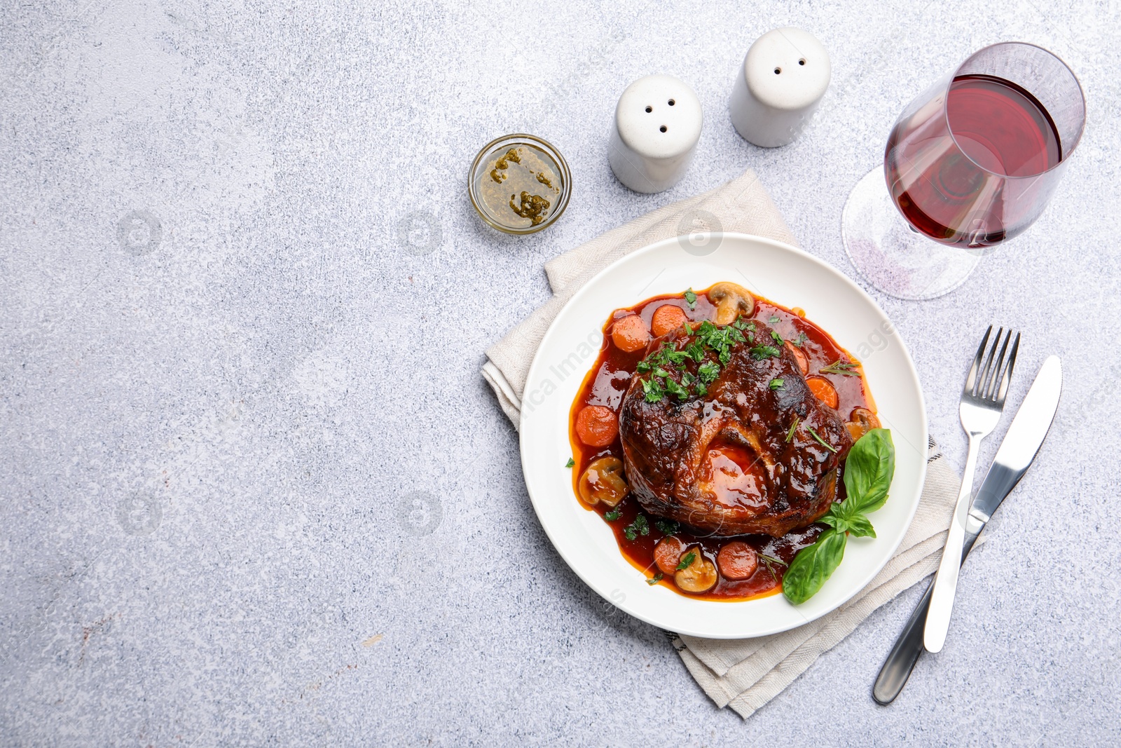 Tasty beef ossobuco with carrot, mushrooms and herbs served on grey textured table, flat lay. Space for text Photo of Tasty beef ossobuco with carrot, mushrooms and herbs served on grey textured table, flat lay. Space for text
