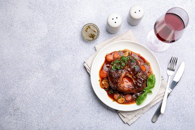 Photo of Tasty beef ossobuco with carrot, mushrooms and herbs served on grey textured table, flat lay. Space for text