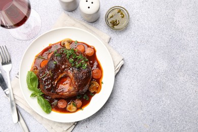 Photo of Tasty beef ossobuco with carrot, mushrooms and herbs served on grey textured table, flat lay. Space for text