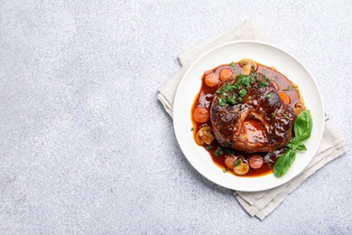 Photo of Tasty beef ossobuco with carrot, mushrooms and herbs on grey textured table, top view. Space for text