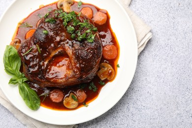 Photo of Tasty beef ossobuco with carrot, mushrooms and herbs on grey textured table, top view