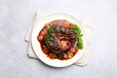 Photo of Tasty beef ossobuco with carrot, mushrooms and herbs on grey textured table, top view