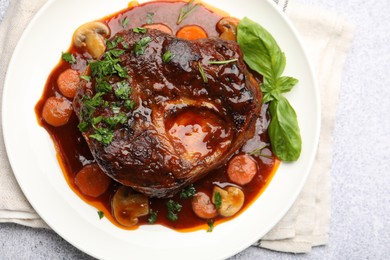 Photo of Tasty beef ossobuco with carrot, mushrooms and herbs on grey textured table, top view