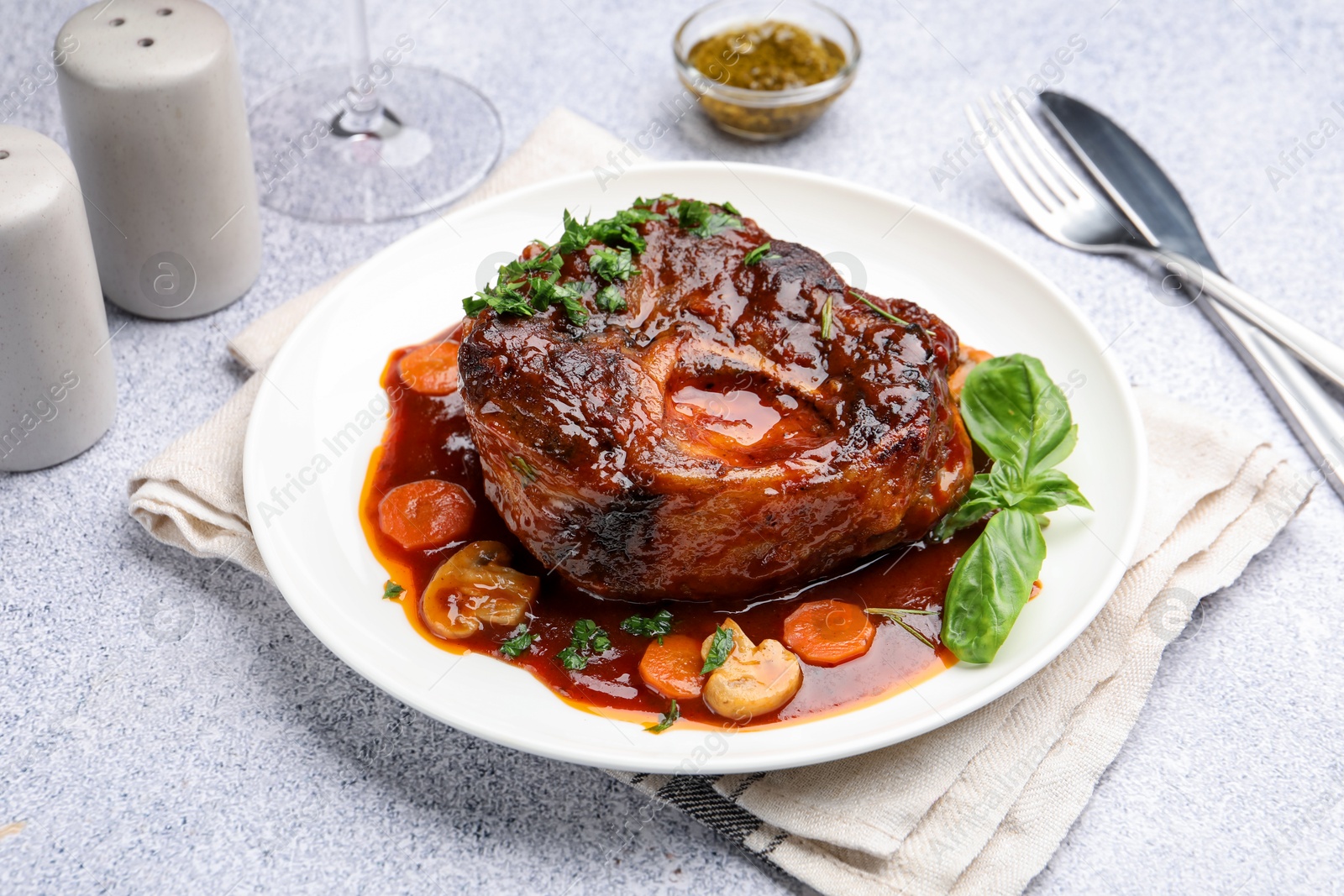 Tasty beef ossobuco with carrot, mushrooms and herbs on grey textured table, closeup Photo of Tasty beef ossobuco with carrot, mushrooms and herbs on grey textured table, closeup