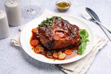 Photo of Tasty beef ossobuco with carrot, mushrooms and herbs on grey textured table, closeup