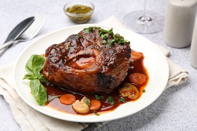 Photo of Tasty beef ossobuco with carrot, mushrooms and herbs on grey textured table, closeup