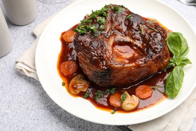 Photo of Tasty beef ossobuco with carrot, mushrooms and herbs on grey textured table, closeup