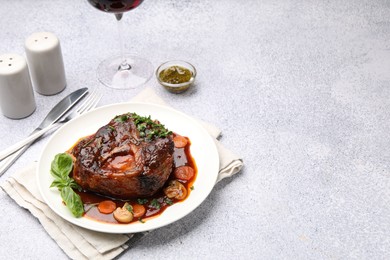 Photo of Tasty beef ossobuco with carrot, mushrooms and herbs on grey textured table, closeup. Space for text