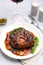 Photo of Tasty beef ossobuco with carrot, mushrooms and herbs on grey textured table
