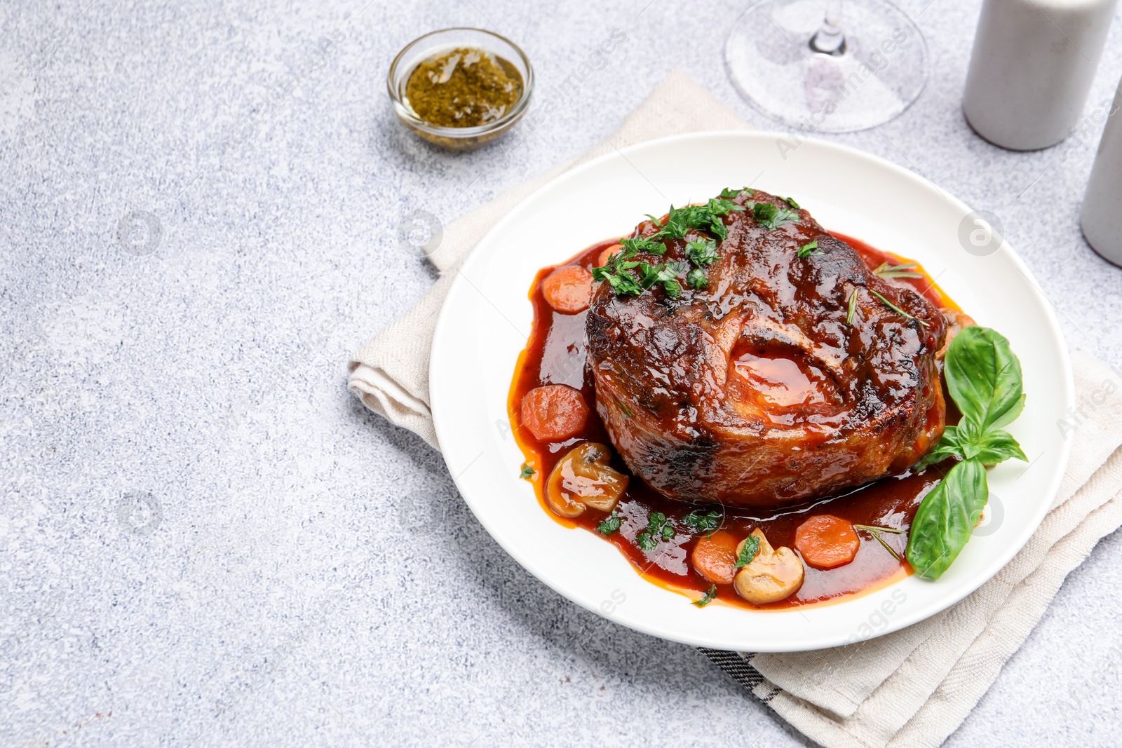 Tasty beef ossobuco with carrot, mushrooms and herbs on grey textured table, closeup. Space for text Photo of Tasty beef ossobuco with carrot, mushrooms and herbs on grey textured table, closeup. Space for text